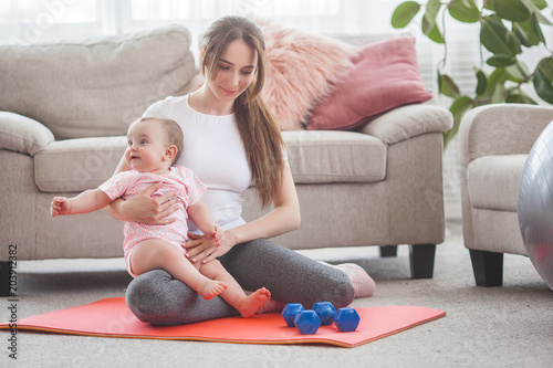 Young pretty mother working out with her little child at home