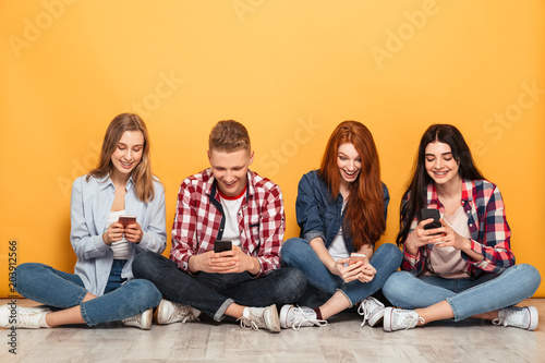 Group of young cheerful school friends using mobile phones