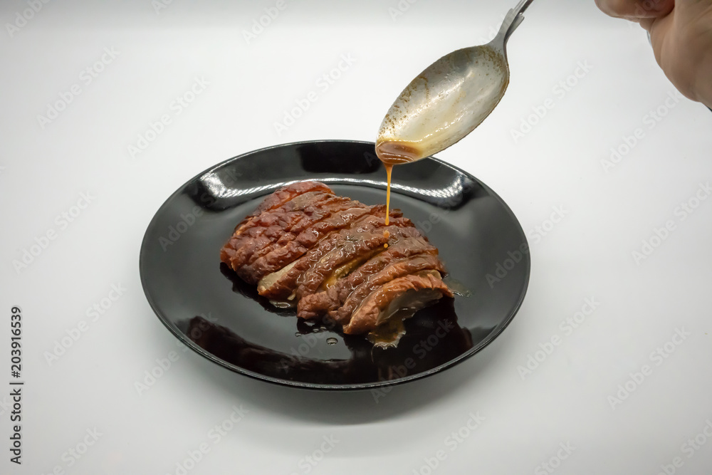 Woman hand holding silver spoon adding sauce on top of roasted duck