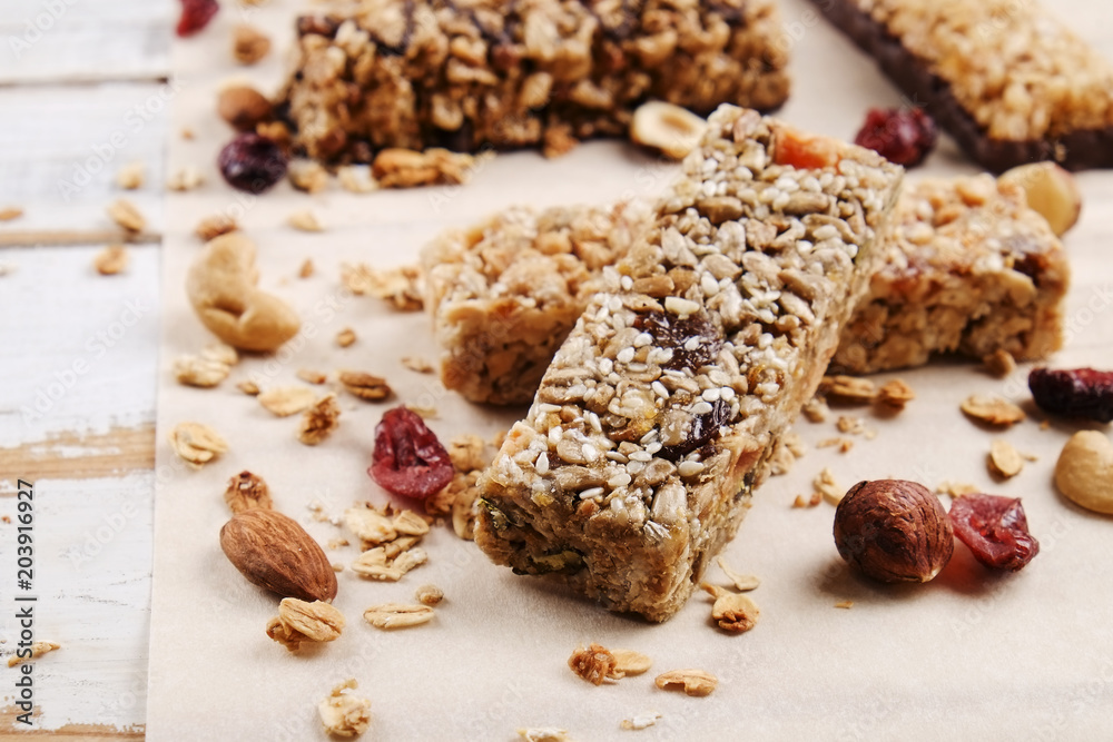 Various granola chocolate energy bars in row with scattered mixed nuts, cereals & dried fruit, grunged white wood table background. Healthy vegan fitness food snack. Top view, copy space, close up. Various granola chocolate energy bars in row with scattered mixed nuts, cereals & dried fruit, grunged white wood table background. Healthy vegan fitness food snack. Top view, copy space, close up.