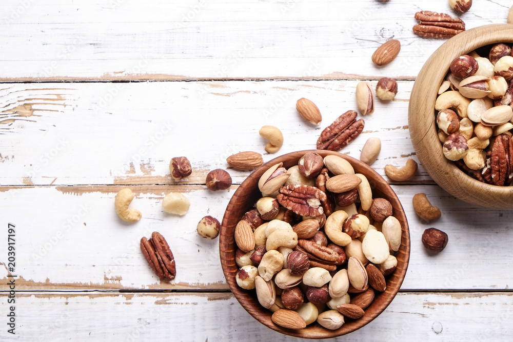 Mixed nuts in wooden bowl and scattered on table. Trail mix of pecan, almond, macadamia & brazil edible nuts with walnut hazelnut on wood textured surface. Background, copy space, top view, close up. Mixed nuts in wooden bowl and scattered on table. Trail mix of pecan, almond, macadamia & brazil edible nuts with walnut hazelnut on wood textured surface. Background, copy space, top view, close up.