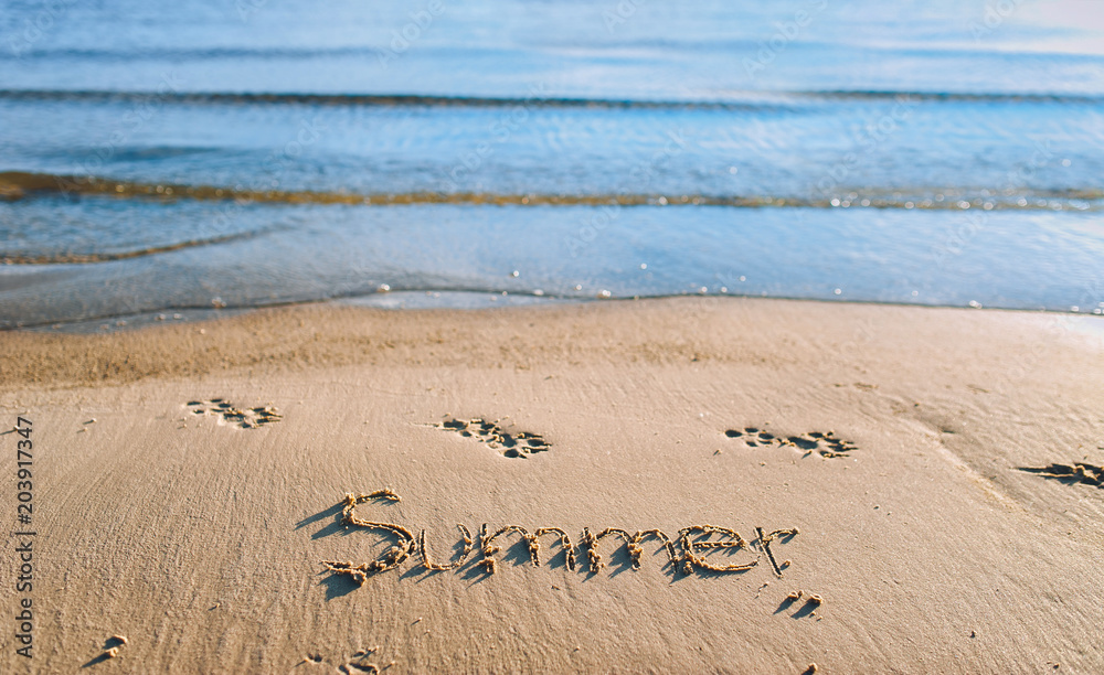 Fototapeta premium The word summer is written in the sand. Blue sea wave. Summer beach concept.