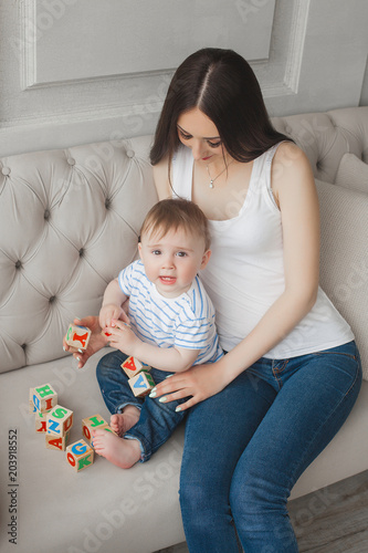 Young pretty mother playing with her little son. Cheerful family having fun indoors with little baby son photo