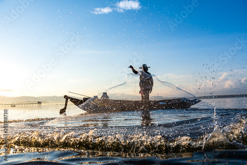 Photo shot of water spatter from fisherman while throwing fishing net on the lake. Silhouette of fisherman with fishing net in morning sunshine. Stop motion water drop.