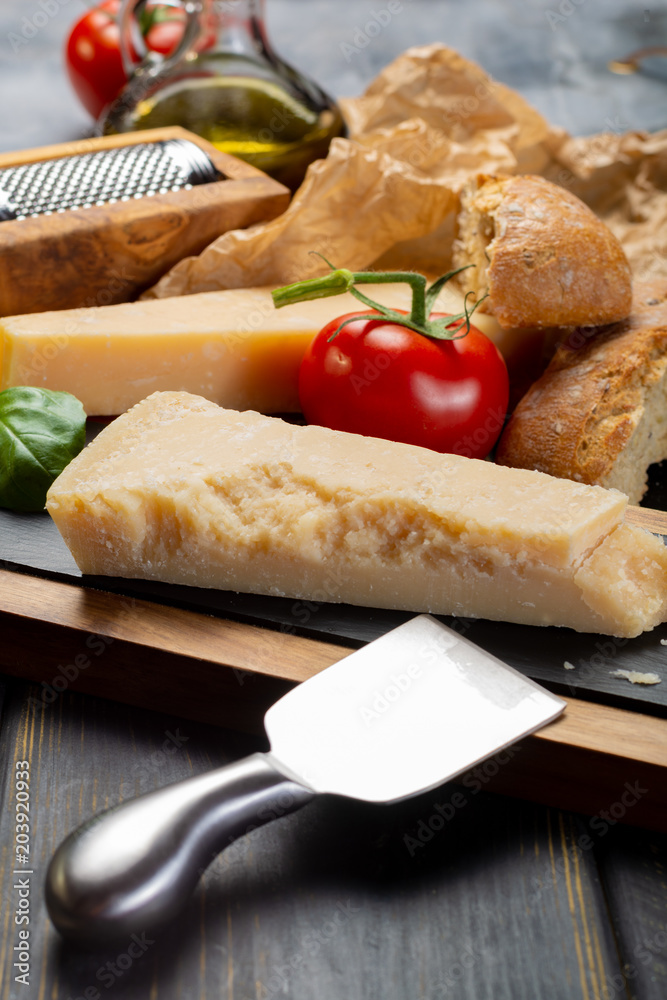 Traditional italian food - aged Italian parmesan hard cheese Parmigiano-Reggiano with cheese knife, tomato, basil, olive oil Traditional italian food - aged Italian parmesan hard cheese Parmigiano-Reggiano with cheese knife, tomato, basil, olive oil