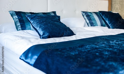 Blue silky hotel room bedding pillows and sheets on bed.