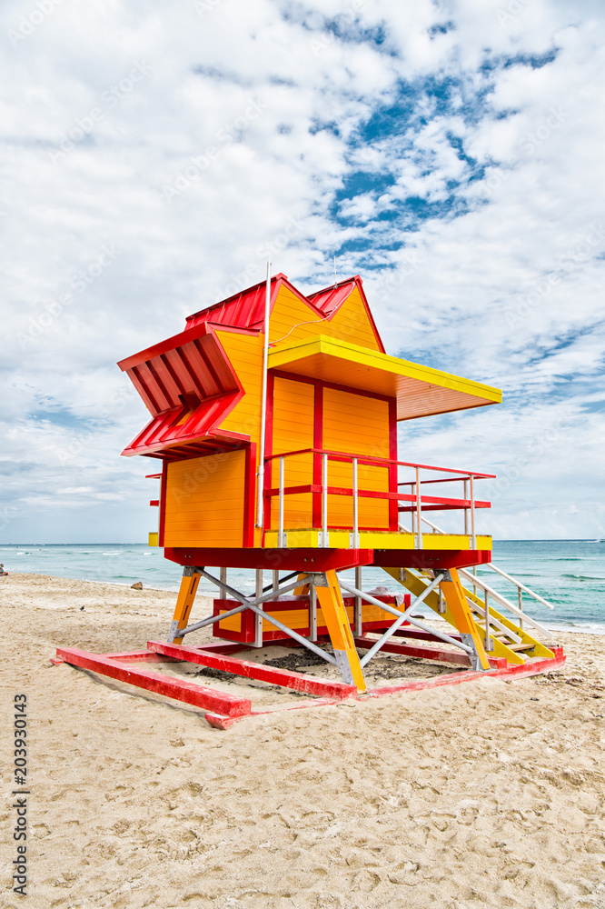 Fototapeta premium Lifeguard house on sand beach in miami, usa. Tower for rescue baywatch in typical art deco style. Wooden house on ocean shore on cloudy sky. Summer vacation concept. Public guarding and safety