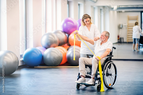 Young woman physiotherapist working with a senior man in wheelchair. photo