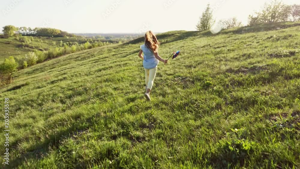 Slow Motion Cute cheerful little girl holding a toy turbine in his hand running away from the camera at sunset Slow Motion Cute cheerful little girl holding a toy turbine in his hand running away from the camera at sunset