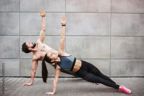 Fototapeta Naklejka Na Ścianę i Meble -  A picture of couple exercising together. They are standing on one hand and reaching up with the other one. They are looking up as well. Couple is concentrated on the exercise.