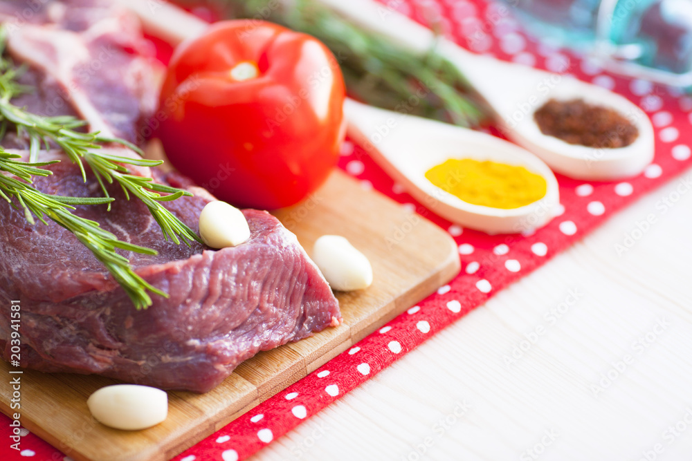 Raw beef meat on the wooden cutting board with vegetables, rosemary and spices. Top view. Close up. Food concept.