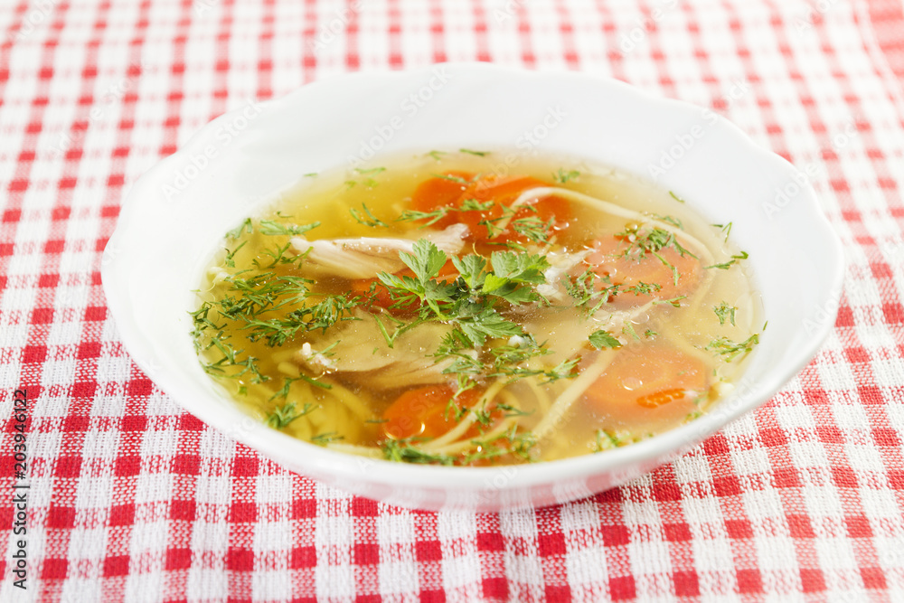 Chicken soup or broth with noodels, chicken meat pieces , carrot slices and herbs in white bowl. Chicken soup or broth with noodels, chicken meat pieces , carrot slices and herbs in white bowl.