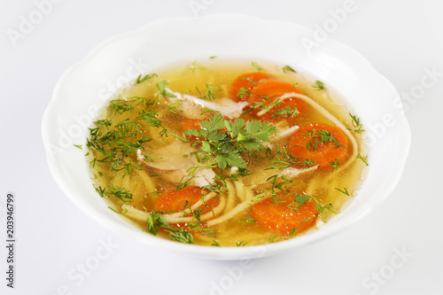 Chicken soup or broth with noodels, chicken meat pieces , carrot slices and herbs in white bowl.