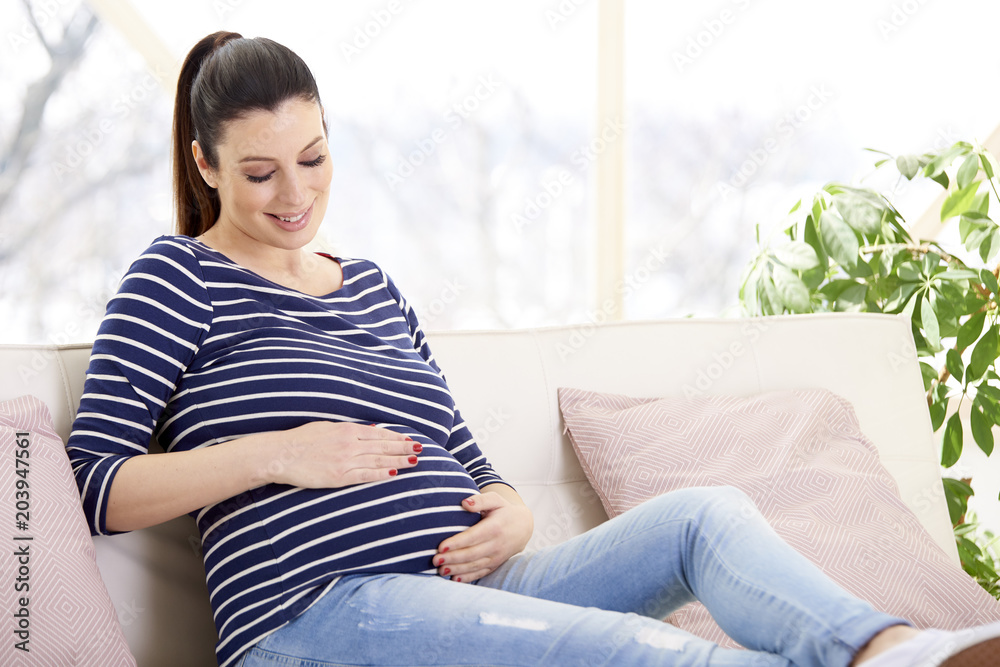 Portrait of beautiful pregnant woman with hands on her baby bump ejoying her pregnancy while relaxing on sofa at home. Portrait of beautiful pregnant woman with hands on her baby bump ejoying her pregnancy while relaxing on sofa at home.
