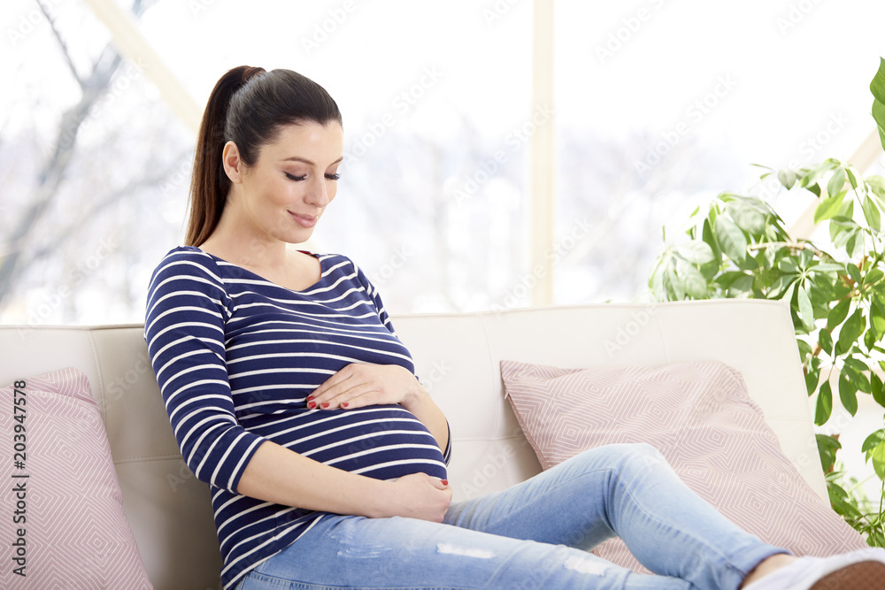 Portrait of beautiful pregnant woman with hands on her baby bump ejoying her pregnancy while relaxing on sofa at home. Portrait of beautiful pregnant woman with hands on her baby bump ejoying her pregnancy while relaxing on sofa at home.