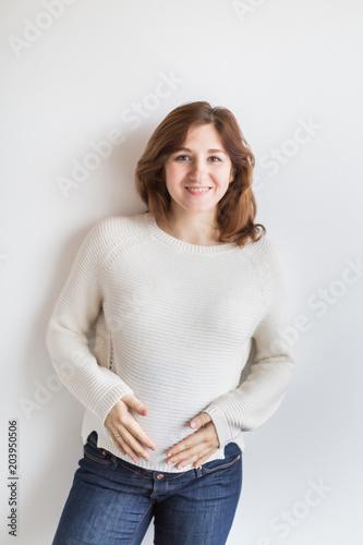 pregnancy, happiness, motherhood concept. there is a lovely young woman with beautiful shining smile and soft not long hair, she is dressed in jeans and sweater