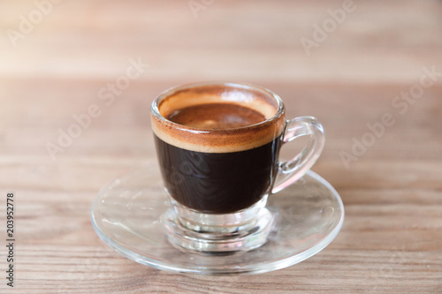 Close-up of espresso coffee in a single shot glass cup with saucer on the wooden table.