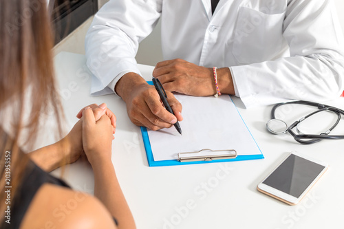 Doctor and patient are discussing about diagnosis. Medical doctor holding a stethoscope, looking at medical form and taking notes. photo
