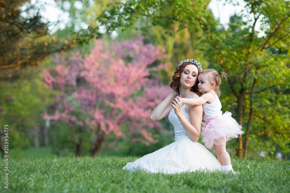 Mom and daughter are two years old sitting on the grass in the park Mom and daughter are two years old sitting on the grass in the park