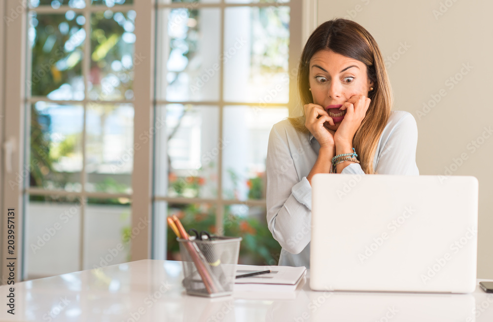Student woman at table with laptop at home terrified and nervous expressing anxiety and panic gesture, overwhelmed Student woman at table with laptop at home terrified and nervous expressing anxiety and panic gesture, overwhelmed