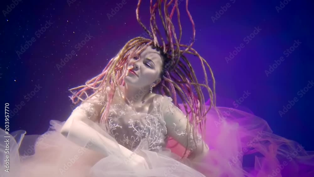 Engaging woman with dreads is floating and posing under the water in pool. Engaging woman with dreads is floating and posing under the water in pool.