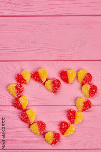 Heart made of sugary candies, top view. Colorful candies forming heart shape on pink wooden background, copy space. Valentines holiday concept.
