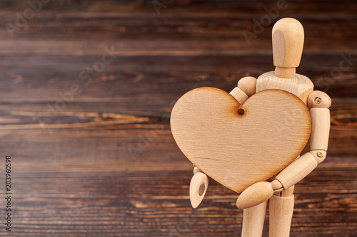 Wooden dummy holding wooden heart. Dummy with blank plywood heart on brown textured background and copy space. photo