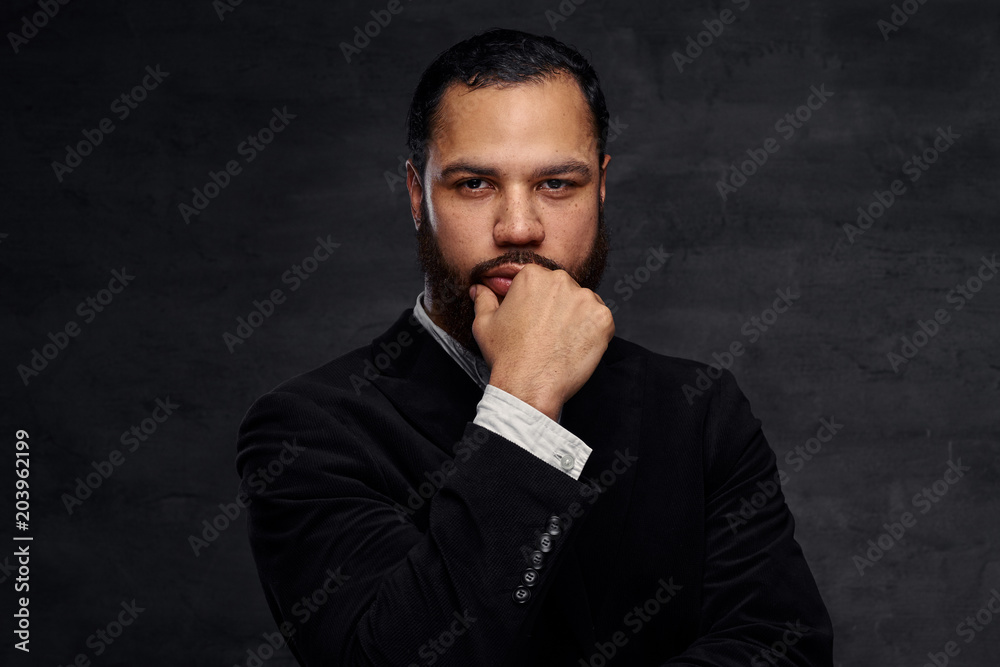 Confident African-American businessman in a black classic jacket, thinking about business while holding hand on chin. Confident African-American businessman in a black classic jacket, thinking about business while holding hand on chin.