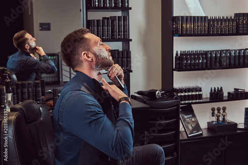 Portrait of a stylish male who himself shaving in a hairdressing salon.