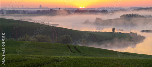 misty sunrise over a lake surrounded by green hills © Mike Mareen
