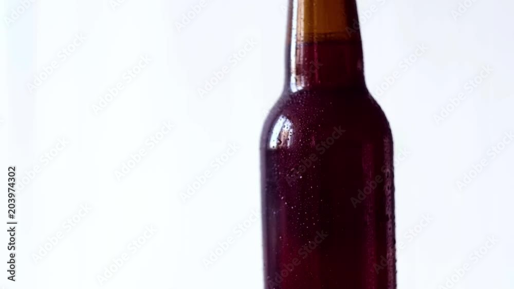 Cold wet brown bottle of beer rotating against light background Cold wet brown bottle of beer rotating against light background