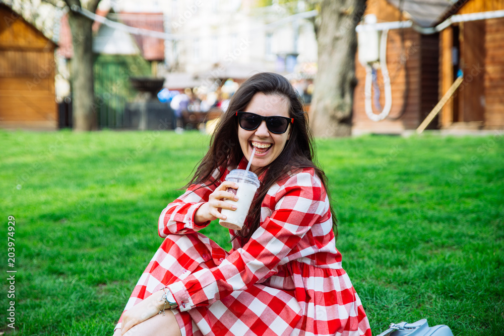 woman in red dress drinking smoothie while sitting on green gras