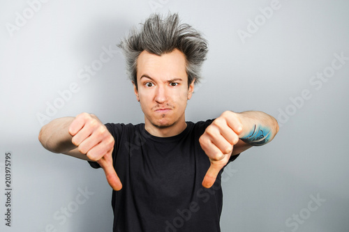 Unshorn and unshaven young guy shows thumbs down, on gray background. photo