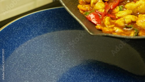 pour stir fried chicken with spicy curry paste , sweet basil, bell pepper, long yard beans , sliced corn from black teflon pan into blue dish