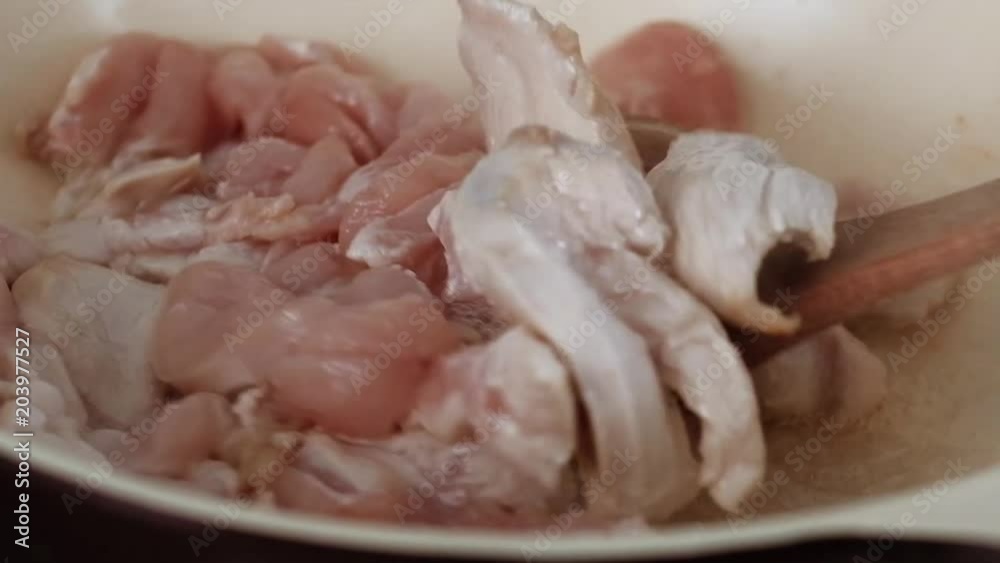Raw pieces of chicken meat on the frying pan. Chicken fillet frying on the frying pan. Roasting of meat fire on a frying pan. Stirring of meat with wood turner spatula Raw pieces of chicken meat on the frying pan. Chicken fillet frying on the frying pan. Roasting of meat fire on a frying pan. Stirring of meat with wood turner spatula