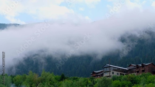 Footage of beautiful green pine forest covered with dense fog with wooden cottages on the foreground, Mestia, Georgia photo