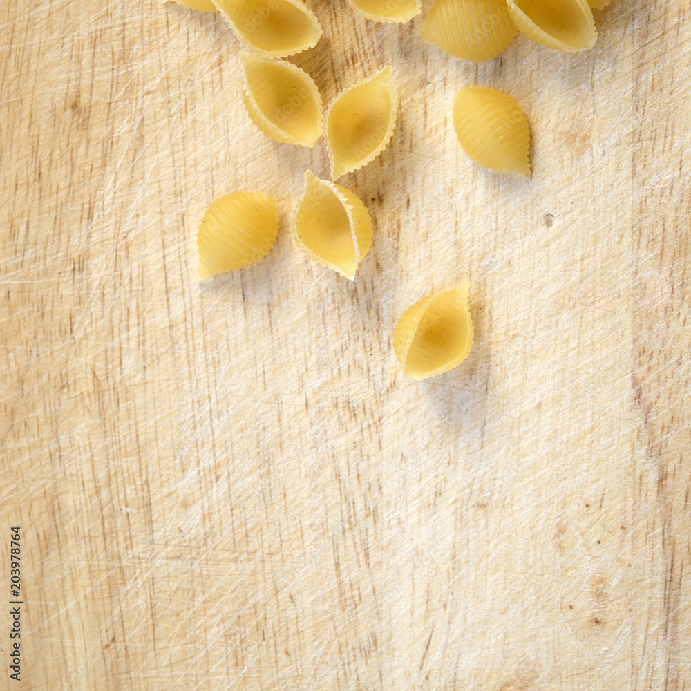Dry shell macaroni on rustic wooden surface close up, conchiglie pasta, basic food of delicious Mediterranean meals Dry shell macaroni on rustic wooden surface close up, conchiglie pasta, basic food of delicious Mediterranean meals