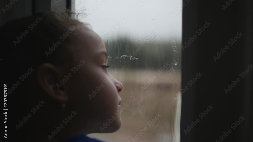 Child looks at the rain behind the window. Stock Footage.