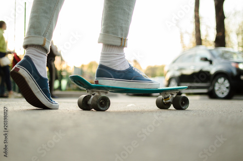 Side view of the young hepcat in blue jeans and canvas skate shoes crossing the road with blue plastic penny skateboard. Concept of the modern transport solutions, commute. photo