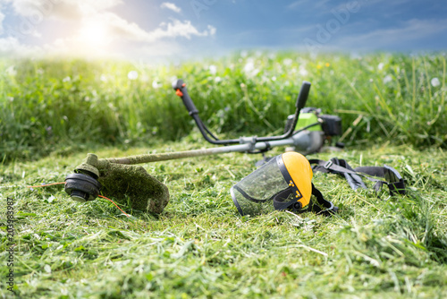 String trimmer and protective face mask on mown grass, sunlight photo