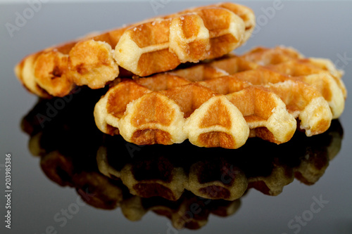 Two golden waffles reflected on a glossy black surface