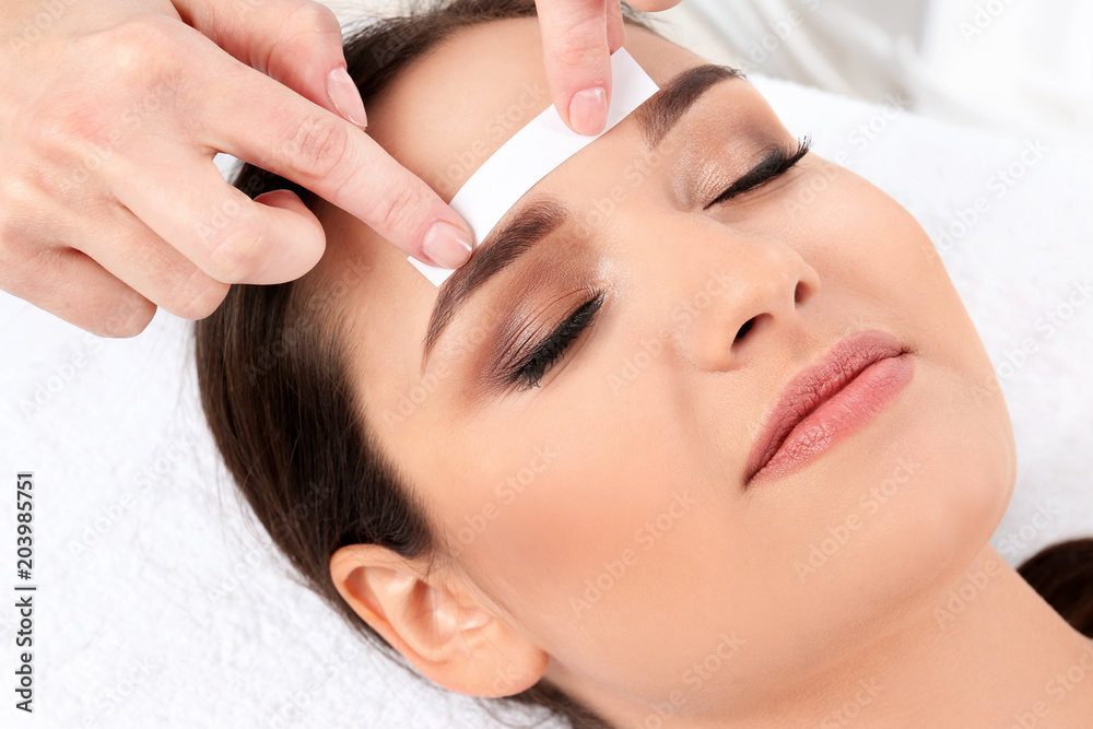 Fototapeta premium Young woman having professional eyebrow correction procedure in beauty salon