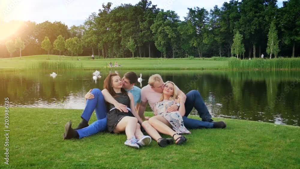 Slow motion video of two couples sitting and kissing by the river at park Slow motion video of two couples sitting and kissing by the river at park