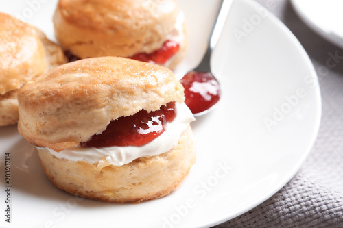 Tasty scones with clotted cream and jam on plate, closeup