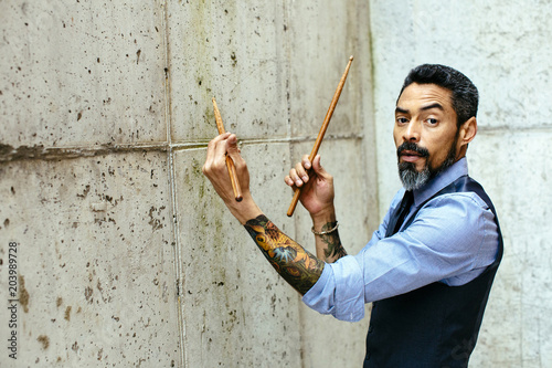 Принти на полотні Portrait of a tattooed man drumming on a concrete wall