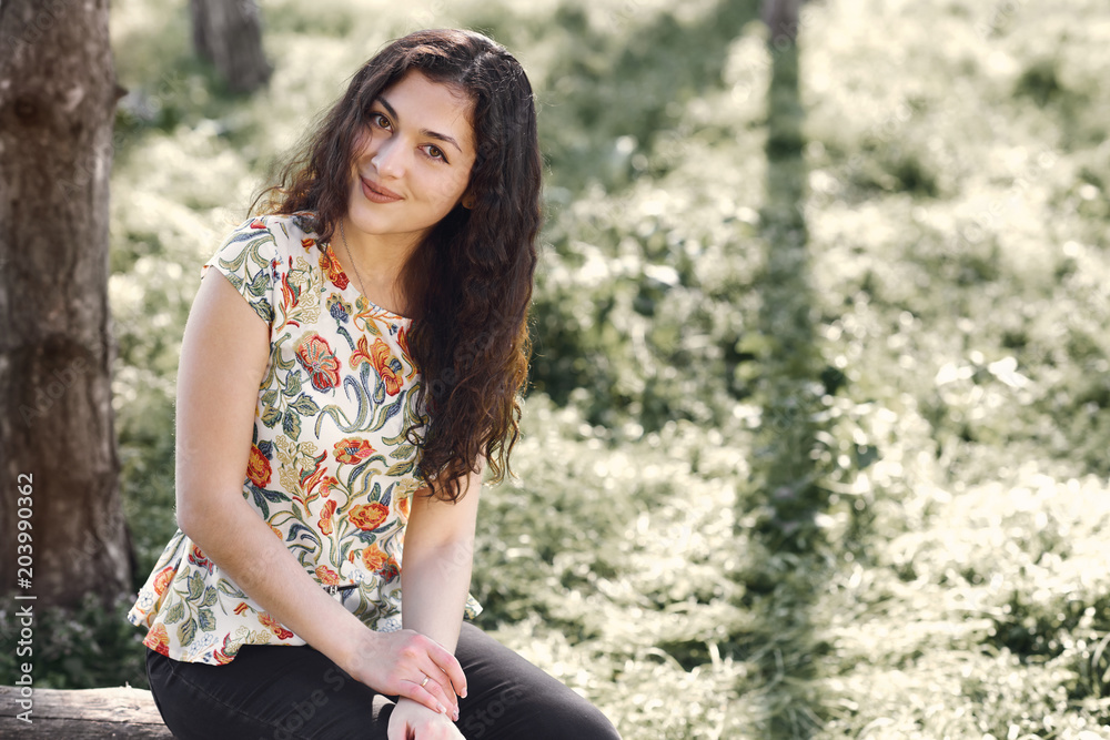 happy young girl sitting on a log in the forest, bright sunlight around, beauty of nature in spring