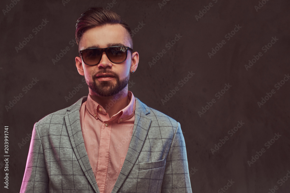 Close-up portrait of a confident stylish bearded man with hairstyle and sunglasses in a gray suit and pink shirt, posing in a studio. Close-up portrait of a confident stylish bearded man with hairstyle and sunglasses in a gray suit and pink shirt, posing in a studio.