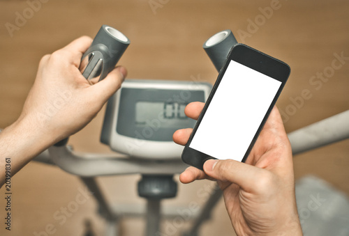 Foto male hands use smart phone with blank touch screen, fitness training on elipsoid