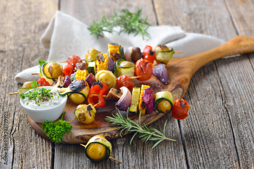 Vegetarisch grillen: Bunte  Gemüsespieße vom Grill mit Kräuterdip  - Grilled skewers with mixed vegetables served  on a wooden cutting board with a vegan herb dip