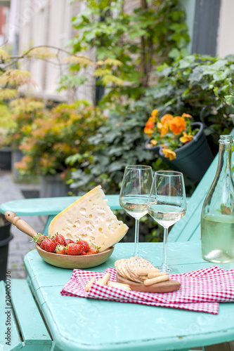 Dutch cheese with holes and strawberry. White wine in a glass and snacks. Food on the balcony. View from above . Place for text. Flowers and plants near the table